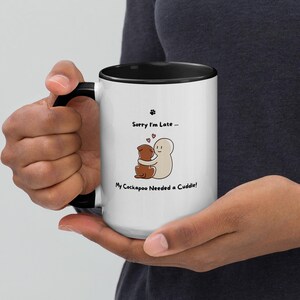 May include: White ceramic mug with a black interior and handle. The mug features the text "Sorry I'm Late..." and "My Cockapoo Needed a Cuddle!" along with a graphic of two hugging cartoon figures and paw prints.