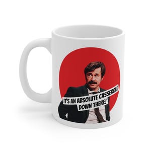 Könnte beinhalten: Weiße Keramik-Kaffeetasse mit rotem Kreis und einem Mann im Anzug. Die Tasse trägt den Text "IT'S AN ABSOLUTE CASSEROLE DOWN THERE!"