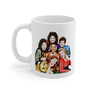 May include: White ceramic coffee mug featuring a colorful image of a group of people. The image depicts six people, with a man in the center, surrounded by five women. The people are smiling and appear to be posing for a photo. The mug has a curved handle.