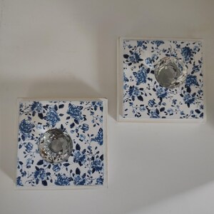 May include: Two square wall hooks featuring a white base with a blue floral pattern and a clear, faceted, crystal-like knob centered on each. The design displays a repeating rose motif in shades of blue against a white background on each square.