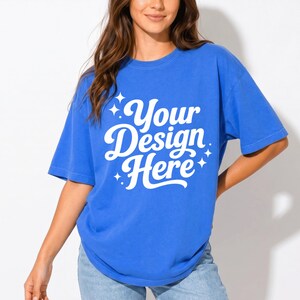 Pode incluir: Uma t-shirt de manga curta azul brilhante com o texto branco Your Design Here numa fonte cursiva arrojada. O design &eacute; acentuado com pequenas estrelas de quatro pontas que rodeiam as letras, criando uma exibi&ccedil;&atilde;o gr&aacute;fica simples e clara.