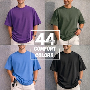 May include: Four t-shirts in different colors: purple, olive green, blue, and black. The image includes the text "44 COLORS" and "COMFORT COLORS". The t-shirts are short-sleeved and appear to be made of a soft material.