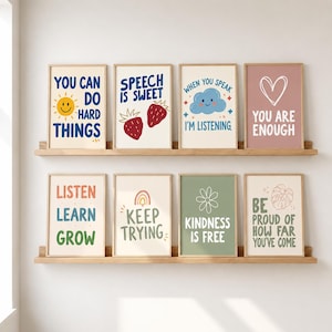 May include: Eight rectangular wall art prints displayed on two wooden shelves. The prints feature motivational text and illustrations including a sun, strawberries, a cloud, a heart, a rainbow, a flower, and a leaf in various pastel colours.