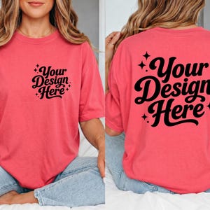 May include: Coral-colored t-shirt with the text "Your Design Here" in a black script font on the front and back. The shirt has short sleeves and a relaxed fit. The text is surrounded by small starburst designs.