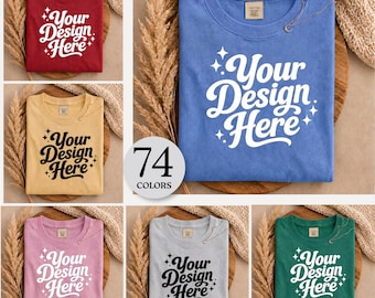 May include: A collection of folded t-shirts in various colors, including red, yellow, blue, pink, gray, and green. Each shirt features the text "Your Design Here" in a stylized font. A circular graphic indicates "74 COLORS".