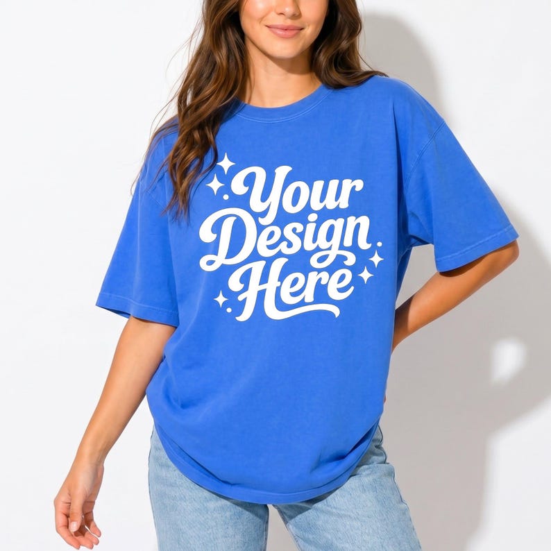 May include: A blue t-shirt with the text "Your Design Here" in white script. The shirt has short sleeves and a crew neck. The model is wearing blue jeans.