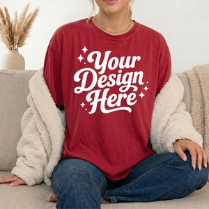 Pode incluir: Uma t-shirt de manga curta vermelho-escura com o texto branco Your Design Here numa fonte cursiva a negrito, acentuada por pequenos gr&aacute;ficos de estrelas brancas de quatro pontas. A t-shirt tem gola redonda e &eacute; usada com cal&ccedil;as de ganga azul-escuras.