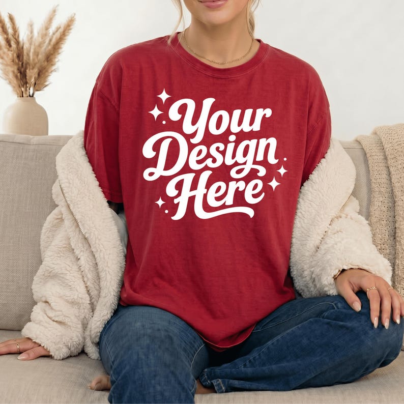 Pode incluir: Uma t-shirt de manga curta vermelho-escura com o texto branco Your Design Here numa fonte cursiva a negrito, acentuada por pequenos gr&aacute;ficos de estrelas brancas de quatro pontas. A t-shirt tem gola redonda e &eacute; usada com cal&ccedil;as de ganga azul-escuras.