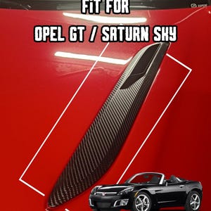 Peut inclure: Un accessoire de voiture en fibre de carbone pour les modèles Opel GT / Saturn Sky. L'image montre une voiture décapotable noire sur fond rouge avec le texte "FIT FOR OPEL GT / SATURN SKY". L'accessoire a un motif texturé.