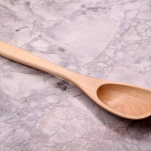 May include: A light-colored wooden spoon with a long handle and a rounded bowl. The spoon is made of a light-colored wood and has a smooth finish. The spoon is designed for cooking and serving.