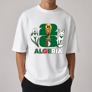 Puede incluir: Camiseta blanca con un dise&ntilde;o que incluye el n&uacute;mero "26", un trofeo dorado, un zorro y la palabra "ALGERIA" en verde y rojo. El dise&ntilde;o tambi&eacute;n incluye una flor y la bandera argelina.