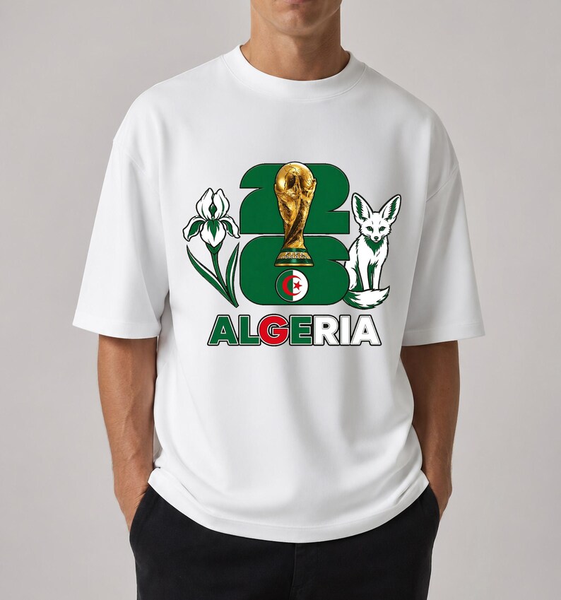 Puede incluir: Camiseta blanca con un dise&ntilde;o que incluye el n&uacute;mero "26", un trofeo dorado, un zorro y la palabra "ALGERIA" en verde y rojo. El dise&ntilde;o tambi&eacute;n incluye una flor y la bandera argelina.