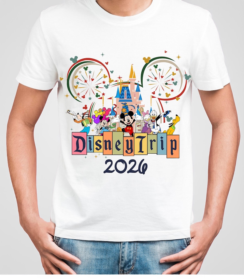 May include: White t-shirt featuring a colorful graphic of Disney characters, a castle, and fireworks. The text "Disney Trip 2026" is displayed below the characters. The design includes Mickey Mouse, Donald Duck, and Goofy.