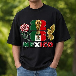 Puede incluir: Camiseta negra con un dise&ntilde;o con el texto "22 23 MEXICO". El dise&ntilde;o incluye un trofeo dorado, una flor roja y blanca, un &aacute;guila dorada y los colores de la bandera mexicana.