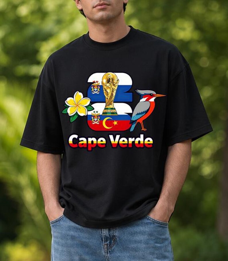 Puede incluir: Camiseta negra con un dise&ntilde;o que incluye el texto "Cape Verde", un trofeo dorado, un p&aacute;jaro y una flor. El dise&ntilde;o incorpora los colores de la bandera de Cabo Verde. La camiseta es de estilo casual y de manga corta.