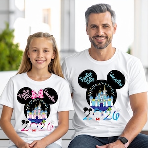 May include: White t-shirts with a Mickey Mouse-inspired design. The design includes a castle, the words "Family Trip Vacation" and the year "2020". The design on the girl's shirt includes a pink bow. The shirts are worn by a girl and a man.