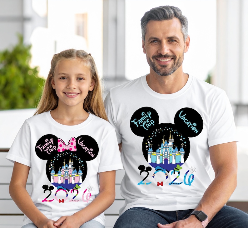 May include: White t-shirts with a Mickey Mouse-inspired design. The design includes a castle, the words "Family Trip Vacation" and the year "2020". The design on the girl's shirt includes a pink bow. The shirts are worn by a girl and a man.