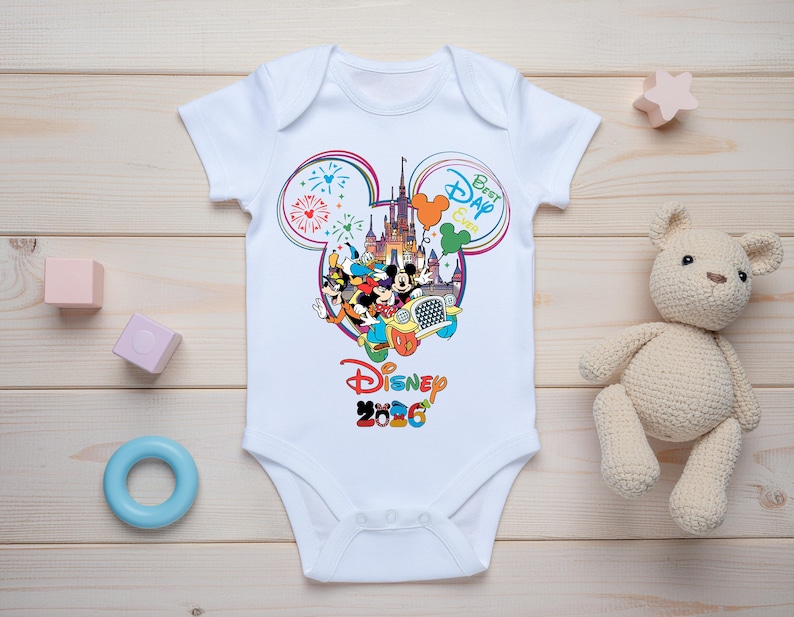 May include: White baby onesie with a colorful Disney graphic. The design features Mickey Mouse, Minnie Mouse, and other characters in front of a castle, with the text "Best Day Ever" and "Disney 2020".
