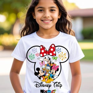 Op de afbeelding: Wit T-shirt met een Disney Trip-ontwerp. Het ontwerp toont Mickey Mouse, Minnie Mouse, Donald Duck, Daisy Duck, Goofy en Pluto, een rode strik met stippen en het jaar 2026.