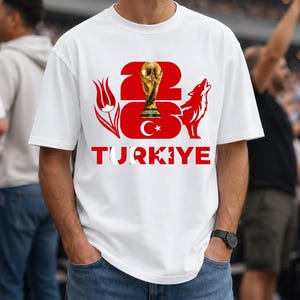 Puede incluir: Camiseta blanca con un dise&ntilde;o gr&aacute;fico que presenta el n&uacute;mero 23, un trofeo dorado, un lobo rojo y la palabra "TURKIYE" en rojo y blanco. El dise&ntilde;o incluye un elemento de la bandera turca. La camiseta es de estilo casual.