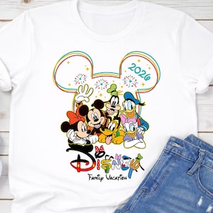 Op de afbeelding: Wit T-shirt met een kleurrijke afbeelding van Disney-personages, waaronder Mickey en Minnie Mouse, Goofy, Donald en Daisy Duck en Pluto. Het ontwerp bevat de tekst "Disney Family Vacation 2026".