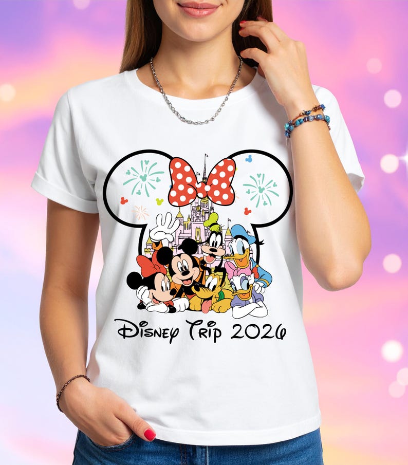 May include: White t-shirt featuring a colorful graphic of Disney characters, including Mickey and Minnie Mouse, Goofy, Donald Duck, and others. The design includes a castle and a red polka-dot bow. The text "Disney Trip 2026" is printed below the characters.
