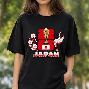 Puede incluir: Camiseta negra con un dise&ntilde;o gr&aacute;fico que dice "2023 JAP&Oacute;N". El dise&ntilde;o incluye un trofeo dorado, la bandera japonesa, flores de cerezo y una grulla. Es una prenda de vestir informal.
