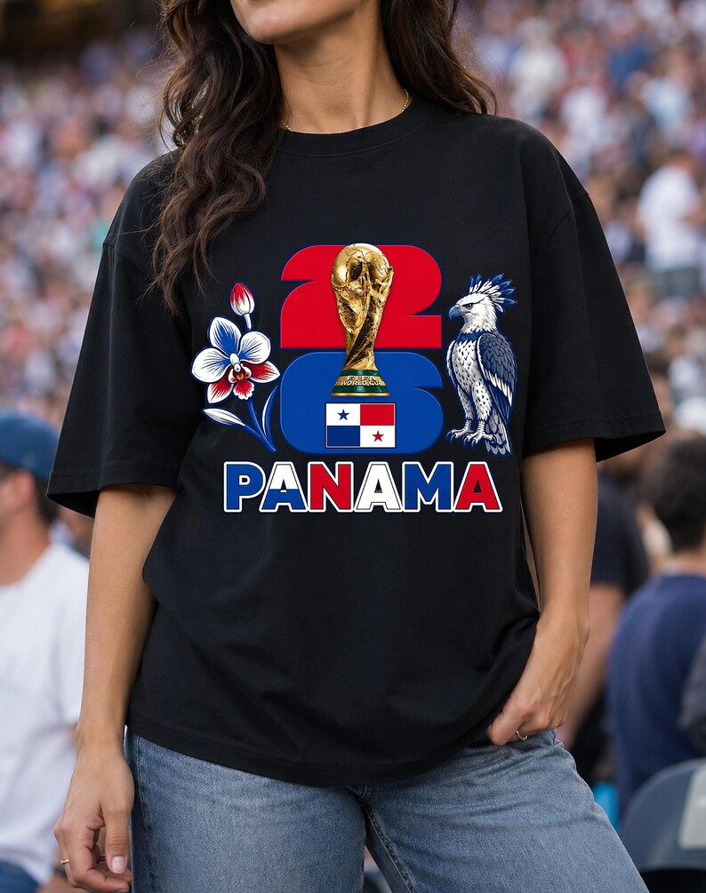 Puede incluir: Camiseta negra con un dise&ntilde;o gr&aacute;fico que presenta el n&uacute;mero "22", un trofeo dorado, una flor azul y blanca, un &aacute;guila estilizada y la palabra "PANAM&Aacute;" en rojo y blanco. La camiseta tiene mangas cortas.