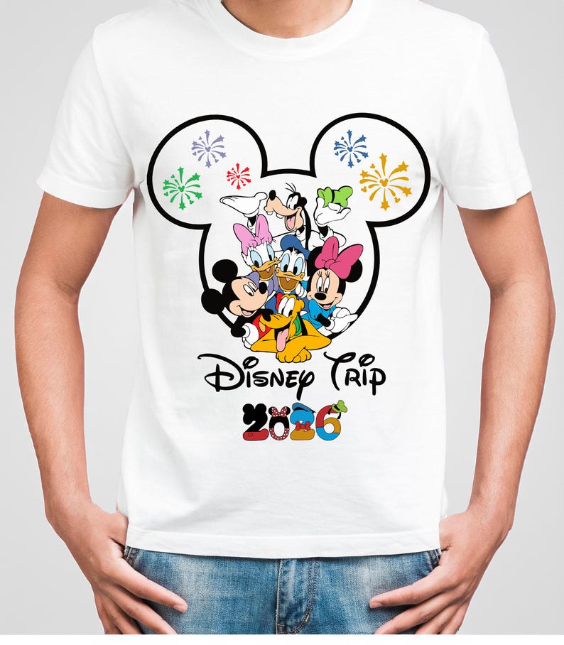 Op de afbeelding: Wit T-shirt met een kleurrijke afbeelding van Disney-personages, waaronder Mickey en Minnie Mouse, Donald Duck en Goofy. Het ontwerp is omlijst door een Mickey Mouse-hoofdvorm en bevat de tekst "Disney Trip 2026".