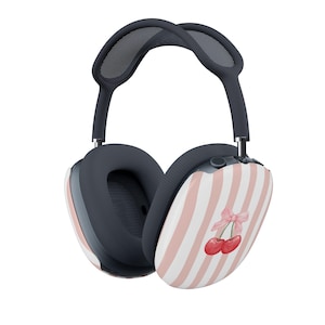 May include: Over-ear headphones featuring a dark grey frame with a mesh headband and ear cushions. The outer ear cups display a light pink and white vertical striped pattern with a small illustration of two red cherries tied with a pink bow.