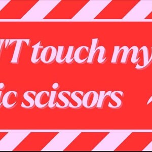 May include: A red sign with the text "DON'T touch my fabric scissors" in white, with a pair of white scissors on the right. The top and bottom of the sign have pink and white diagonal stripes.