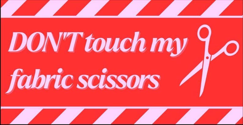 May include: A red sign with the text "DON'T touch my fabric scissors" in white, with a pair of white scissors on the right. The top and bottom of the sign have pink and white diagonal stripes.