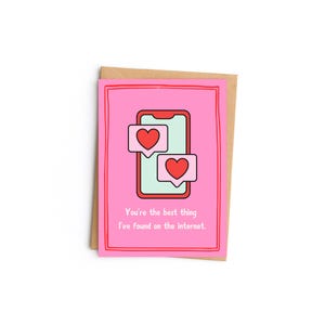 Puede incluir: Una tarjeta de felicitación rosa con un sobre marrón. La tarjeta presenta un gráfico de teléfono inteligente con dos burbujas de diálogo en forma de corazón. El texto de la tarjeta dice: "Eres lo mejor que he encontrado en Internet."