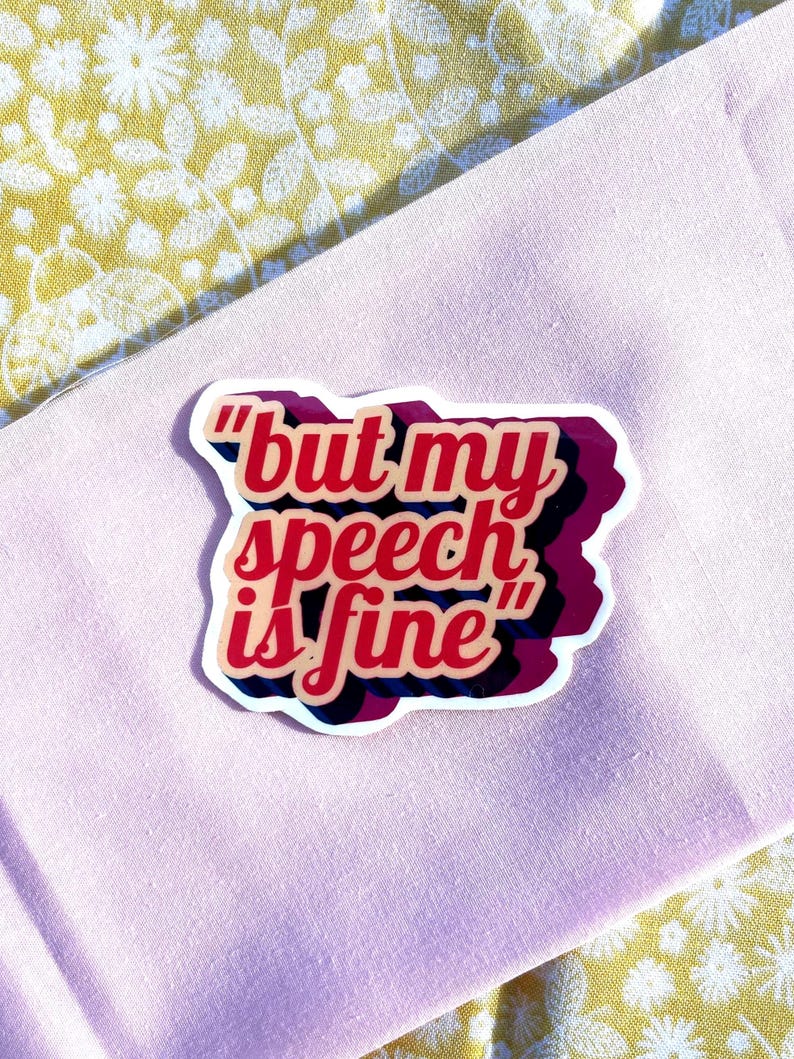 May include: A sticker with the phrase "but my speech is fine" in red, pink, and black lettering. The sticker is on a light pink fabric, with a yellow floral patterned fabric in the background.
