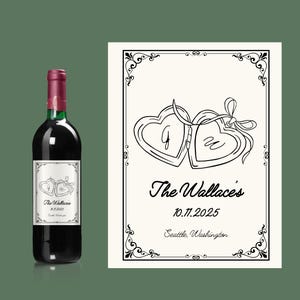May include: A bottle of red wine with a custom label featuring two interlocking heart-shaped lockets. The label includes the names "The Wallace's", the date 10.11.2025, and the city "Seattle, Washington".