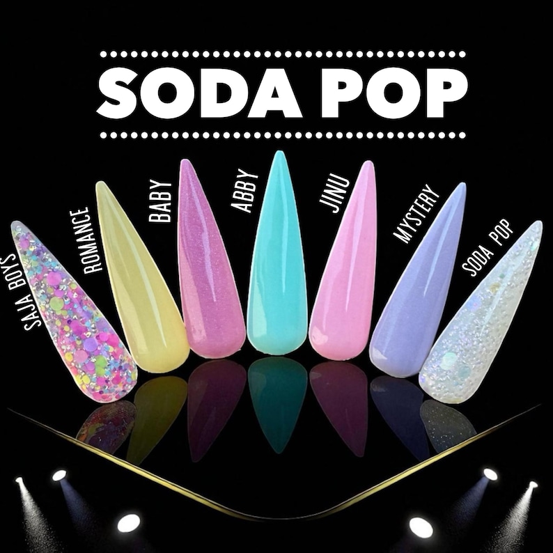May include: A collection of eight long, pointed acrylic nail tips in various colors, including pink, yellow, blue, and glitter. The text "SODA POP" is displayed above the nails, with individual names like "BABY" and "ABBY" labeling each tip. The background is black.