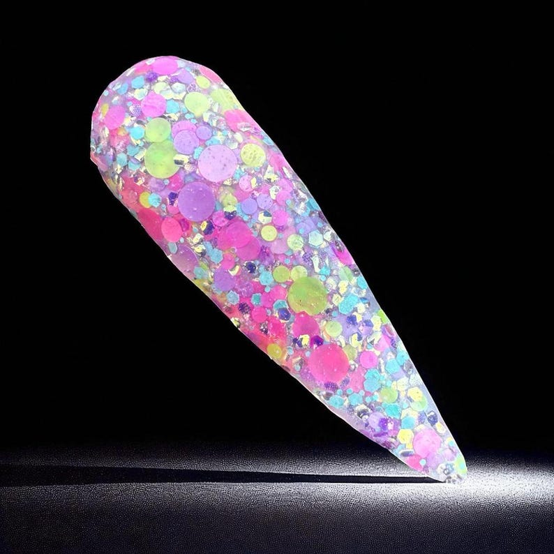 May include: A single, long, pointed nail with a clear base, filled with colorful glitter. The glitter includes pink, purple, green, and blue circular and hexagonal shapes. The nail is set against a black background.
