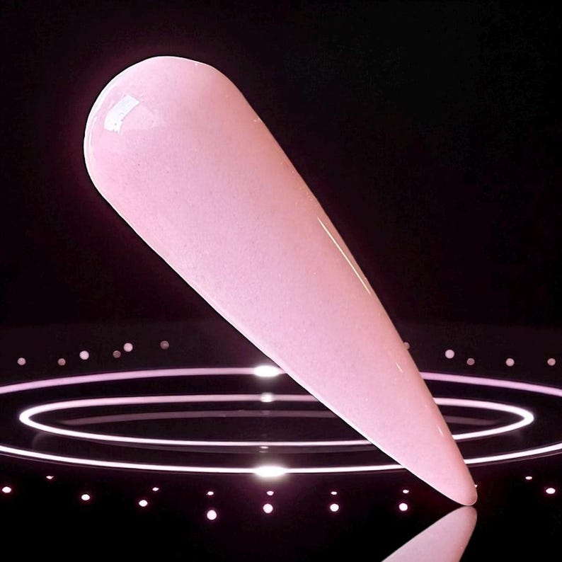May include: A single, elongated, light pink nail with a glossy finish. The nail is set against a dark background with a series of concentric circles and small, illuminated dots, creating a modern aesthetic.