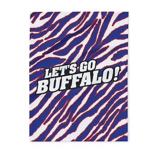 May include: A white and blue patterned textile with red accents. The design features a zebra stripe pattern with the text "LET'S GO BUFFALO!" in white and black.