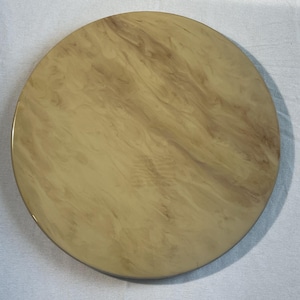 May include: A round, decorative serving tray with a marbled pattern in shades of beige and brown. The tray has a smooth, glossy finish and a dark brown edge. The tray is approximately 12 inches in diameter.