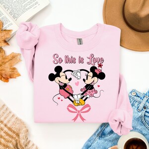 Pu&ograve; includere: Una felpa rosa chiaro con un'immagine di Topolino e Minnie che si tengono per mano a forma di cuore. Il testo "So this is Love" &egrave; sopra i personaggi. Un fiocco rosa &egrave; in basso. La felpa &egrave; realizzata in materiale morbido.