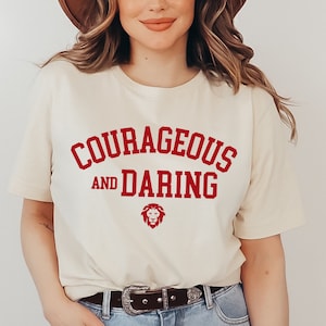 May include: A white t-shirt with the text "Courageous and Daring" in red lettering. A red lion graphic is below the text.