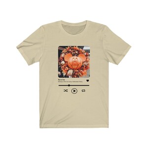 May include: A beige t-shirt with a black and white image of Mickey Mouse as a pumpkin on a wreath. The image is in a square frame with a play button, a rewind button, and a forward button. The text "Boo to You" and "Mickey's Not So Scary Halloween Party" are below the image.