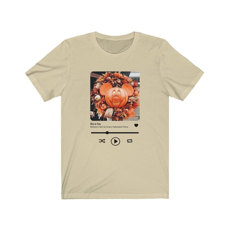 May include: A beige t-shirt with a black and white image of Mickey Mouse as a pumpkin on a wreath. The image is in a square frame with a play button, a rewind button, and a forward button. The text "Boo to You" and "Mickey's Not So Scary Halloween Party" are below the image.