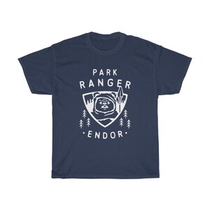 May include: A navy blue t-shirt with a white graphic of a character from Star Wars, a spear, and trees. The text "Park Ranger Endor" is printed on the shirt.