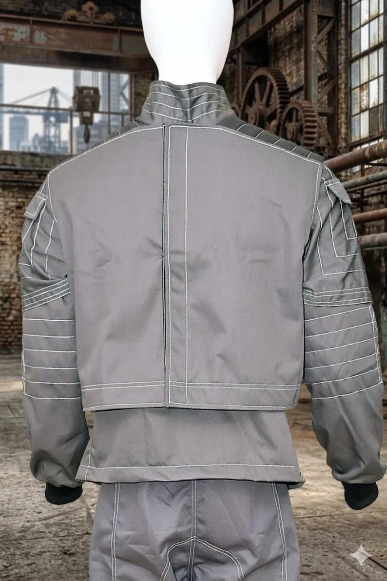 May include: Gray jacket and pants set with white stitching details. The jacket has a stand-up collar, multiple pockets, and horizontal stitching on the sleeves. The pants are visible at the bottom of the image. The outfit is displayed on a mannequin.