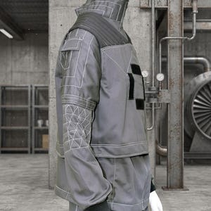 May include: Gray workwear-style jacket and pants set on a mannequin. The jacket features white stitching, black patches, and a quilted shoulder design. The pants have black patches and white stitching. The mannequin is wearing black gloves.