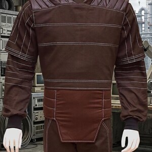 May include: Brown jumpsuit with white stitching details. The outfit features a high collar, padded shoulders, and horizontal stripes across the torso. The long sleeves have black cuffs, and the pants are also brown.