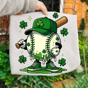 May include: A cartoon baseball character wearing a green cap and trainers, holding a bat. The baseball is decorated with green shamrocks and dripping green paint. The design is on a white background.