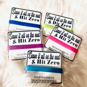 May include: Multiple white cards with the text "Leave it all on the mat & Hit Zero" are shown. Each card features a coloured band in blue, green, pink, purple, and teal. The cards are presented on a white, fluffy surface.